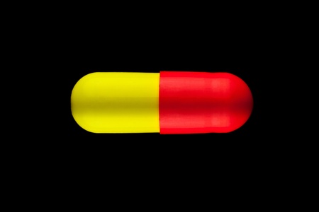 One red and yellow pills isolated on black background の写真素材