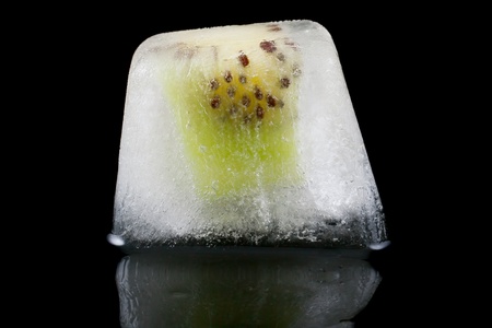 Slice of kiwi fruit frozen in ice on a black background の写真素材
