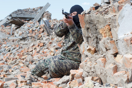 Military camouflage with a rifle on a background of bombed buildings.の写真素材
