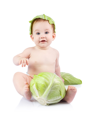 Beautiful little baby on a white background with green cabbage.の写真素材