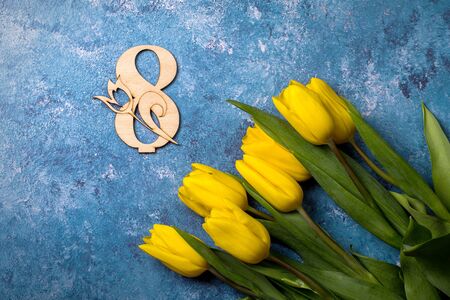 A bouquet of yellow tulips on a blue background, next to a wooden number 8.の写真素材