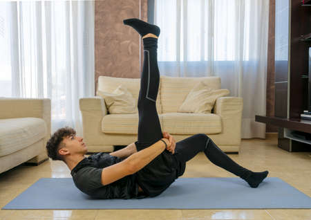 Young man with black sportswear practicing exercise in the living room at home on blue matの写真素材