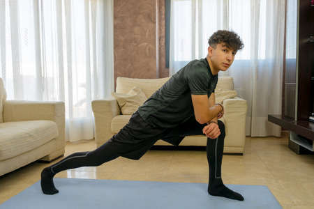 Young man with black sportswear practicing exercise in the living room at home on blue mat