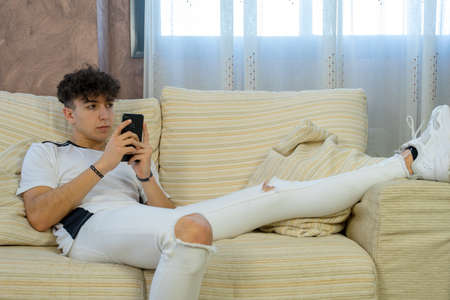 Young man posing on a white sofa in his living roomの写真素材