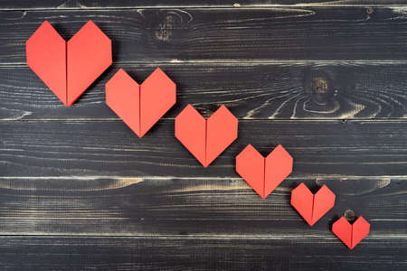 Red origami hearts of different sizes in composition on weathered black wooden background