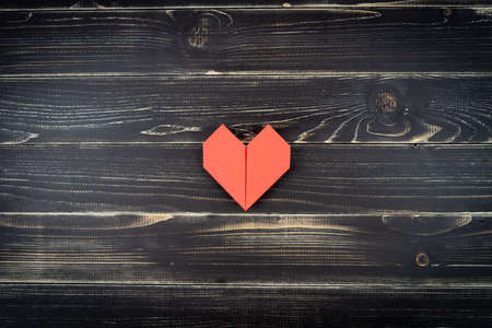 Red origami hearts of different sizes in composition on weathered black wooden background