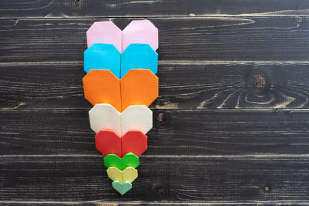 Origami hearts of different colors and sizes in composition on weathered black wooden background
