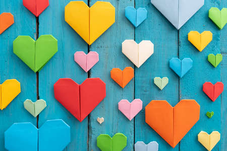 Origami hearts of different colors and sizes in composition on weathered blue wooden backgroundの写真素材