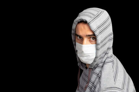 Young man in a gray hoodie and mask to prevent coronavirus posing with black backgroundの写真素材