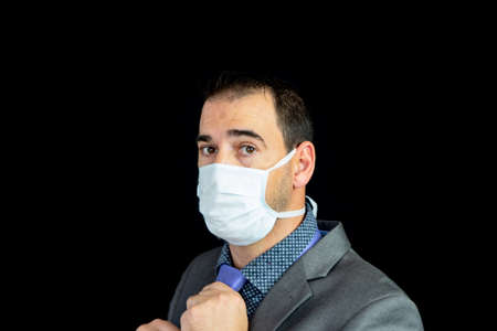 Young man in suit and mask to prevent coronavirus posing with black backgroundの写真素材