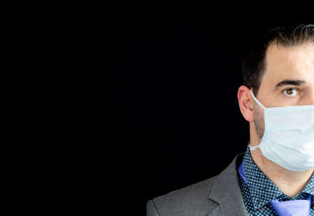 Young man in suit and mask to prevent coronavirus posing with black backgroundの写真素材