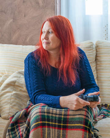Woman with red hair playing the game console on the white sofa in he living room