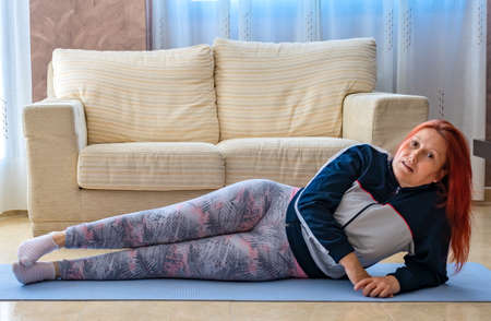 Redhead adult woman wearing sports clothes doing fitness on mats indoors. Health conceptの写真素材