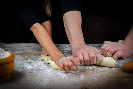 Hands of man and girl kneading bread dough on a wooden table with black background. Craft conceptの写真素材