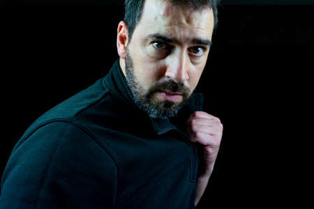 Portrait of bearded man dressed in black sweatshirt on a black background in challenging attitude.Loneliness conceptの写真素材