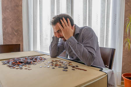 Bearded man in white and black shirt doing puzzle in his living room. Entertainment conceptの写真素材