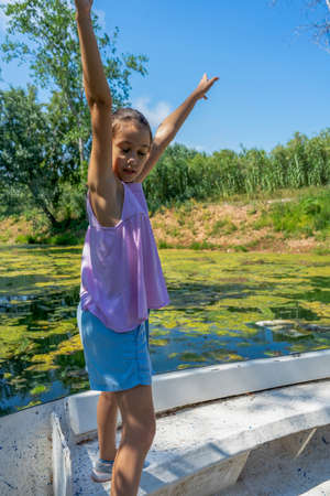 Beautiful little girl with her hair up and dressed in pastel colors posing fun riding on a white boat in the freshwater pond of Clot de la Mare de Deu in Burriana. Tranquility conceptの写真素材
