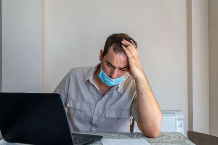 Bearded man dressed in beige shirt and wearing a mask to protect himself from coronavirus looking at...