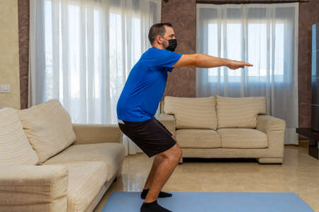 Bearded man in low shape exercising with black and blue sportswear and a mask to prevent coronavirus...