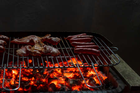 View of a half-done night barbecue with sausages, hamburgers, pork and bacon. Selective focusの写真素材