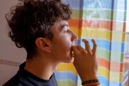 Attractive young man with curly hair eating a sweet in the kitchen of his home. Food concept