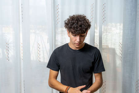 Attractive young man with curly hair wearing black t-shirt posing on white curtains background....