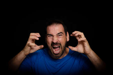 Bearded man wearing blue t-shirt with angry expression posing on black background. Disposal conceptの写真素材