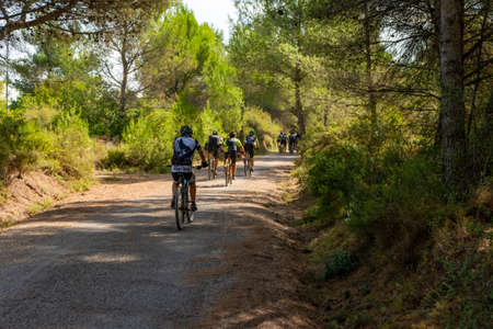 Algimia de Alfara, Spain 10/08/2020: Group of middle-aged cyclists riding on a natural road on a sunny autumn dayのeditorial素材