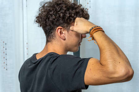 Attractive young man with curly hair wearing black t-shirt posing on white curtains background....