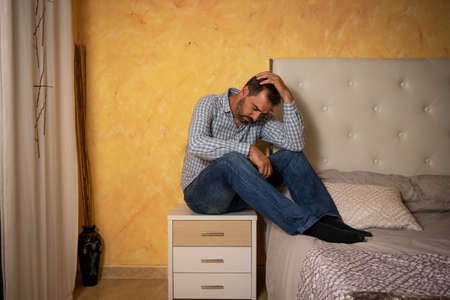 Attractive bearded man depressed and upset in the bedroom at home. Dramatic 30-40 year old lifestyle...