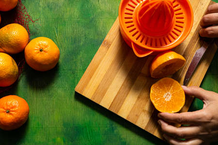 Man's hands making orange juice with a manual juicer on an old wooden background in green tones. Mediterranean diet conceptの写真素材