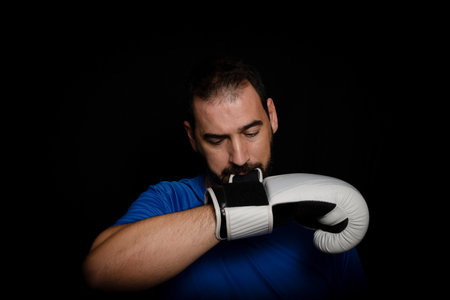 Bearded man dressed in blue t-shirt and with boxing gloves posing on black background. Sport conceptの写真素材