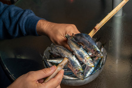 Strong men's hands preparing a skewer of fresh salty sardines in a glass bowl with a cane. Healthy...