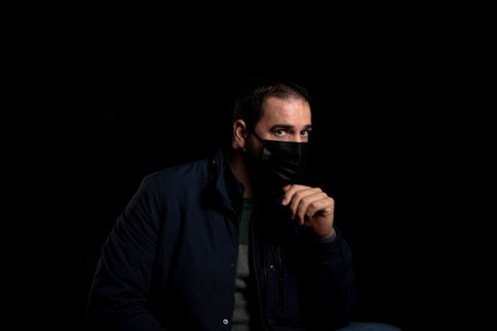 Bearded man equipped with a mask to protect himself from coronavirus wearing a blue jacket posing...