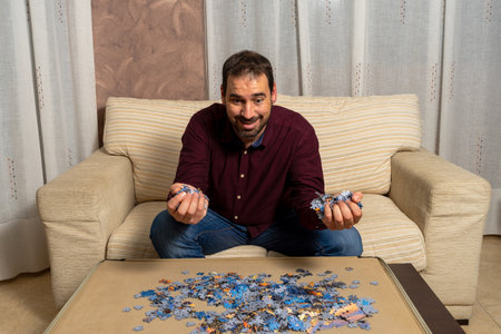 Young man with beard sitting on the couch at home doing puzzle. Entertainment concept