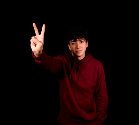 Attractive young man making the victory symbol on a black studio background. Optimism concept