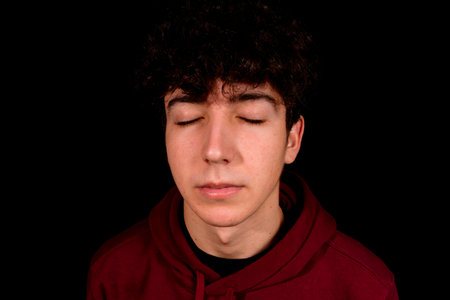 Attractive young man with curly hair posing on black background. Fashion concept