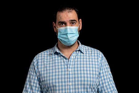 Portrait of bearded man dressed in white and blue plaid shirt posing worried isolated on black...