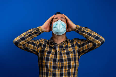 Bearded man in a yellow and blue plaid shirt posing with a surgical mask to protect  with his hands...
