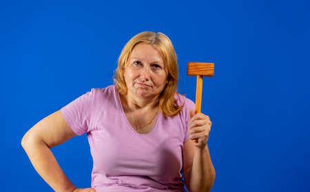 Pretty middle aged woman posing with a kitchen wooden mallet isolated on blue studio background. Warning conceptの写真素材