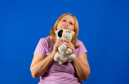 Pretty middle-aged woman playing with a stuffed puppy on blue studio background.の写真素材