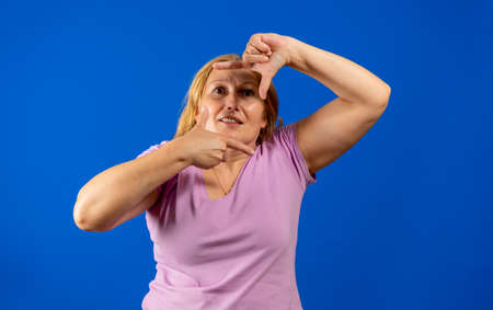 Middle aged woman making a frame shape with hands, trying to focus as if it were a cameraの写真素材