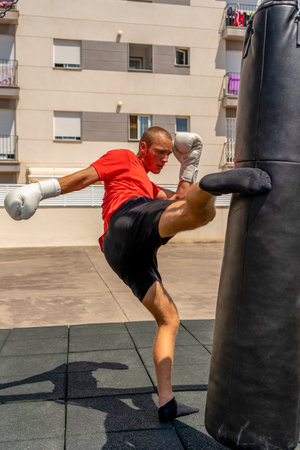 Young caucasian man kicking a punching bag hanging on the street, he trains hard to improve. Contact sport. Training conceptの写真素材