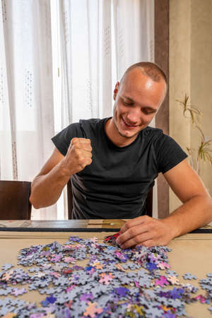 Handsome man doing a puzzle alone and enjoying a relaxing day at home. Man in his 20s sitting on the...