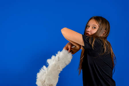 Pretty preteen girl posing with a cleaning duster in her hand isolated on blue studio background. Cleaning conceptの写真素材