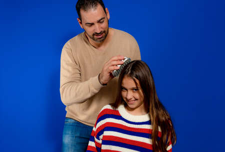 Happy millennial single father combing hair of adorable little school daughter. Smiling young carrying daddy looking after small girl, preparing her for school or kindergarten, helping with hairstyle.の写真素材