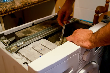 Mans hands repairing a broken washing machine that has a family unable to wash everyones clothesの写真素材