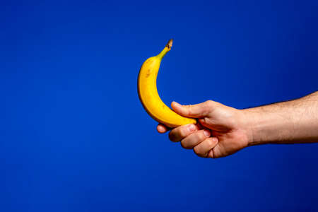 Hand holds banana. Isolated on blue background. Alpha.の写真素材