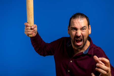 Cooking is a passion. Portrait of young handsome gesturing with a rolling pin with aggressive face expression while standing over blue background with copy spaceの写真素材