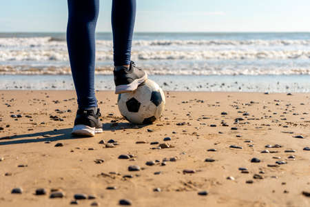 Legs of a girl stepping on a soccer ball on the beach with the sea in the background, she watches the sea while pursuing her dream of becoming a soccer playerの写真素材